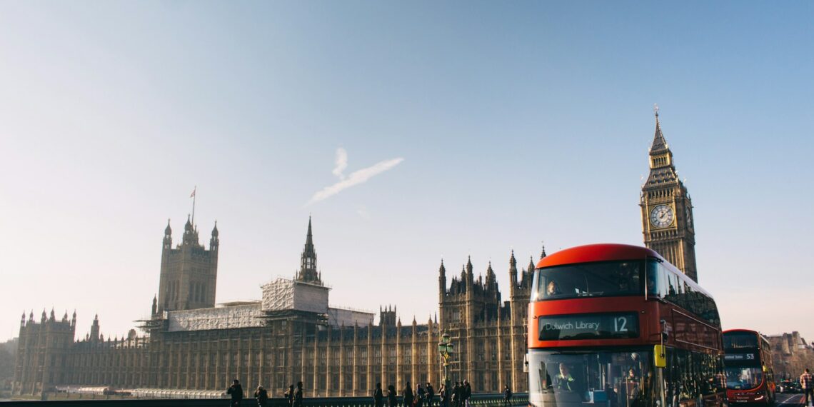 red double-decker bus passing Palace of Westminster, London during daytime